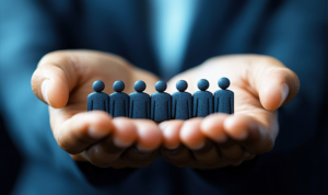 Businessperson cupping their hands around small human figure icons, representing customer protection and care